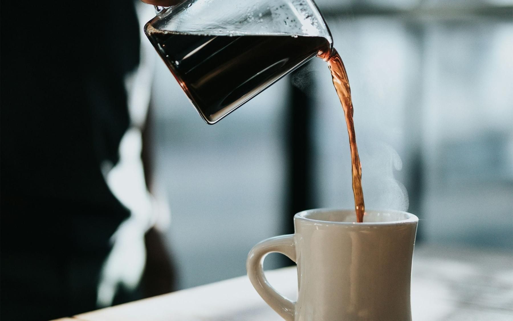 a person pouring a carafe of coffee into a cup