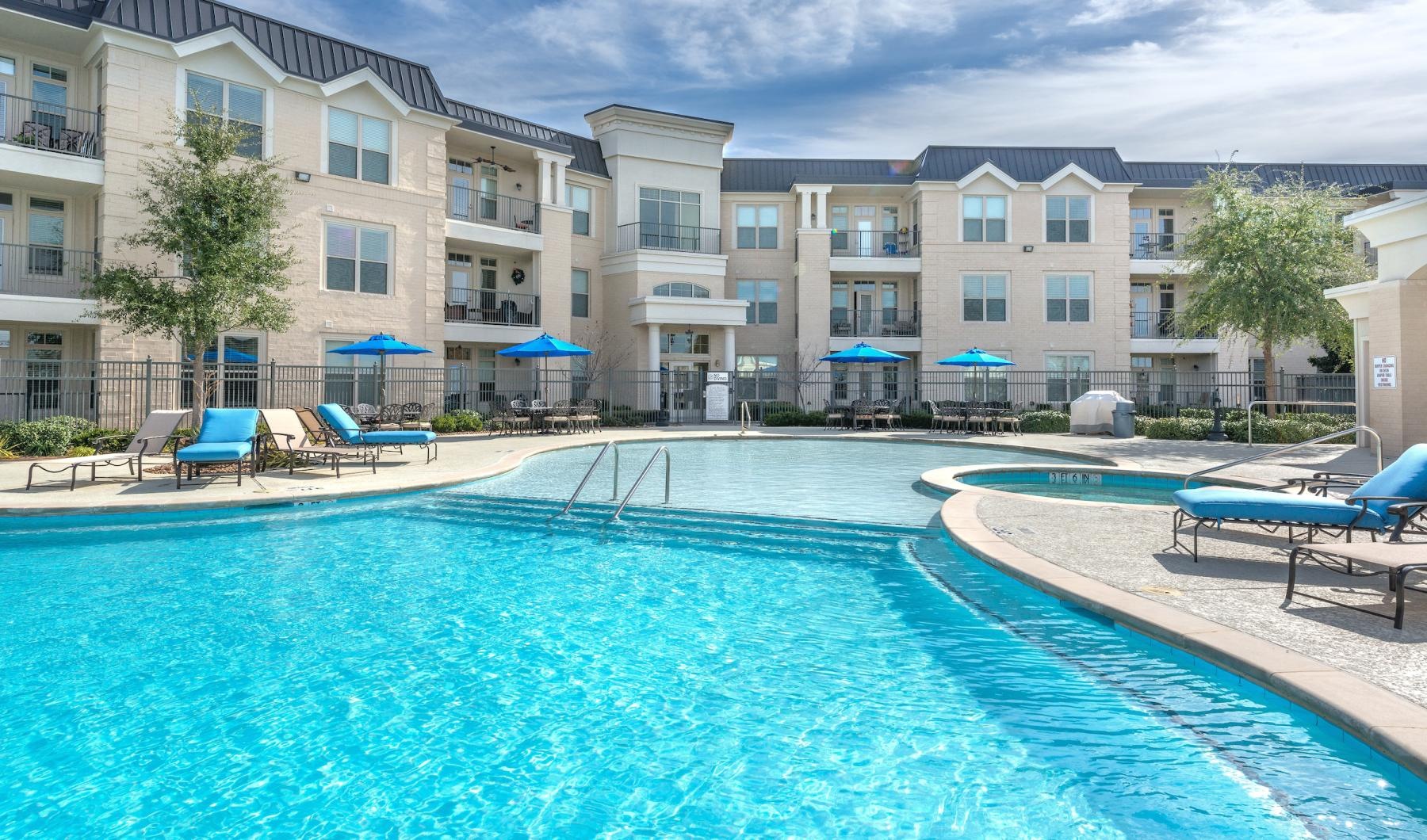 Large sparkling blue pool with a large deck and lounge chairs 