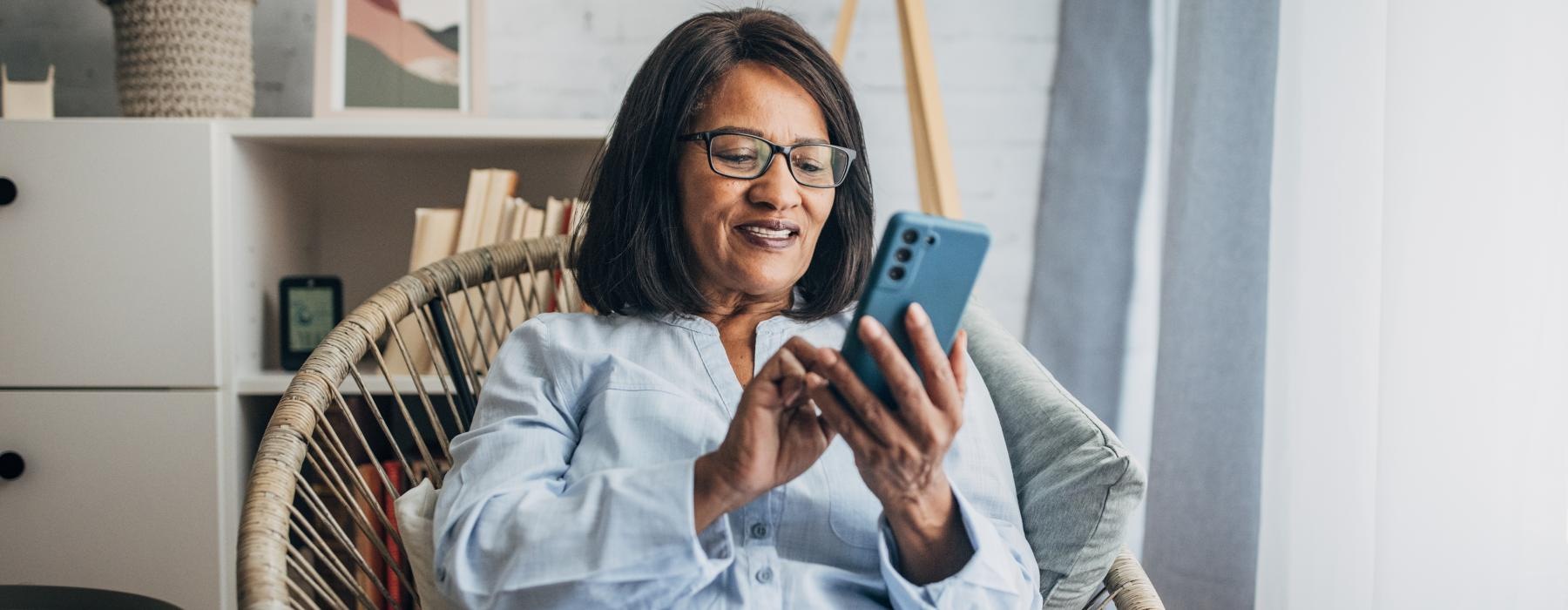 Woman sitting in a chair looking at her phone and smiling 