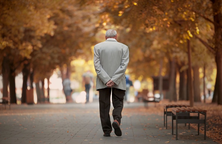 A senior adult walks by himself down a park.