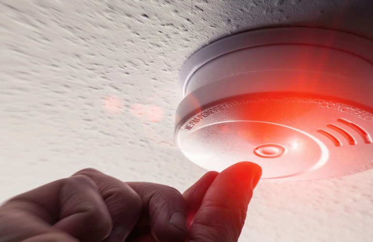 Close up of a hand testing a smoke alarm in a home.