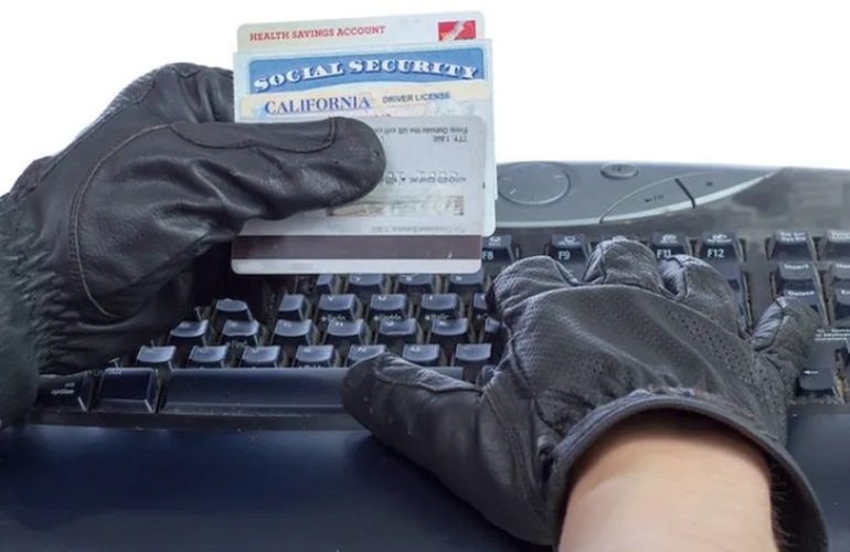 Close up image of a thief holding IDs and credit cards in front of a keyboard.