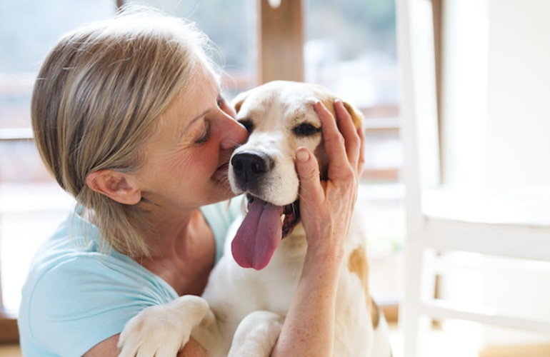 A senior lady kisses her dog in her house.