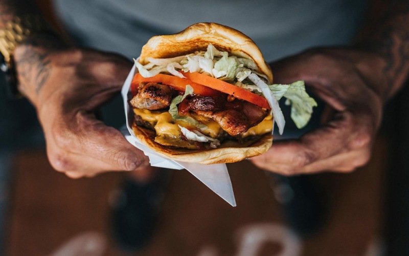 man holds a thick, juicy burger with both hands