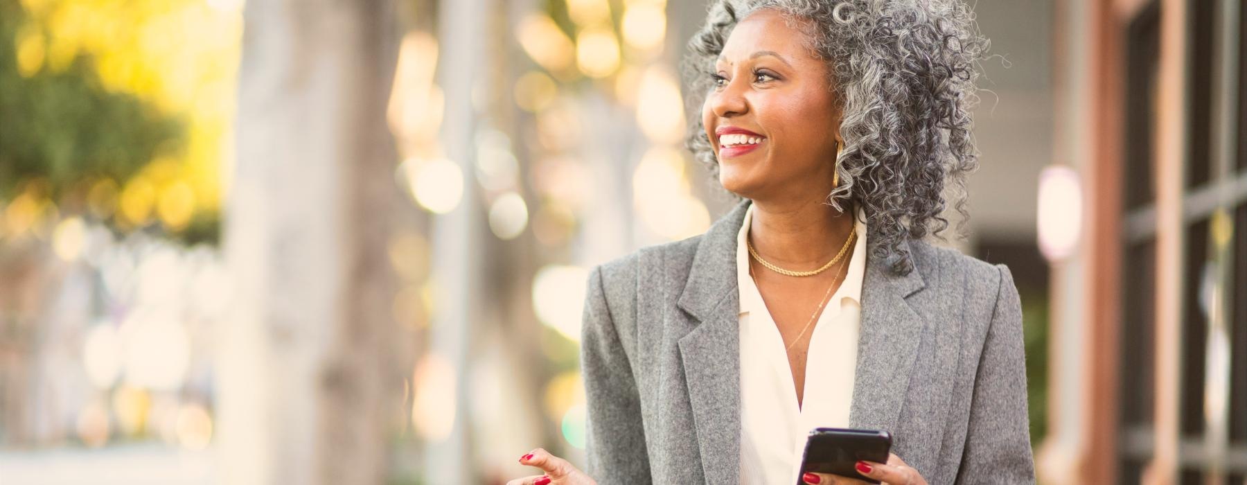 Woman walking on a sidewalk near shops smiling 