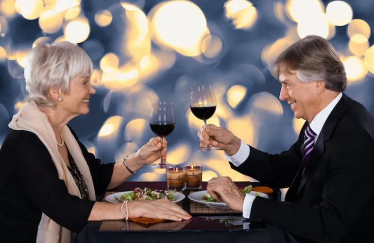 A senior adult couple toast wine glasses while out on a date at a restaurant.