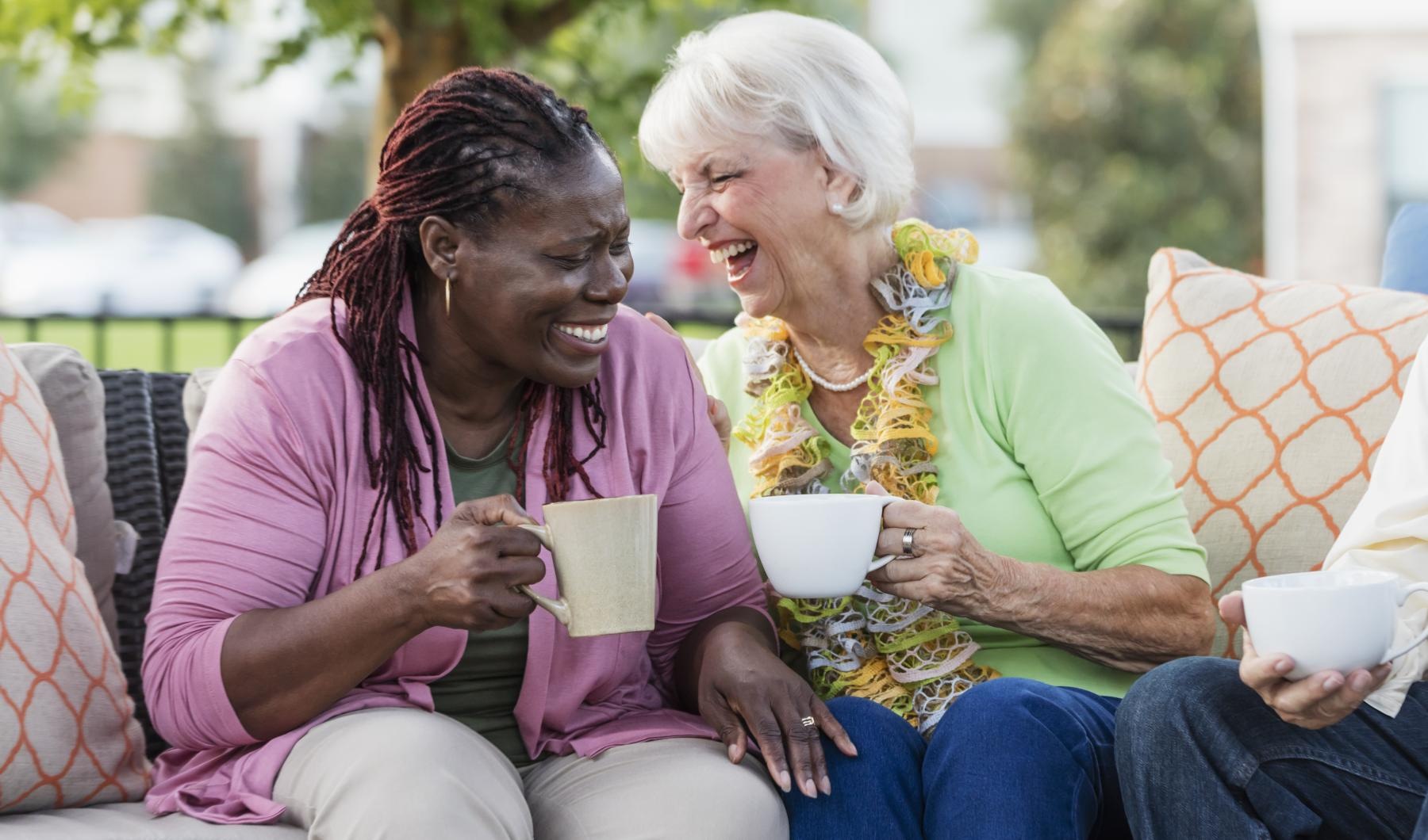 Lifestyle Friends sitting outside laughing and drinking coffee