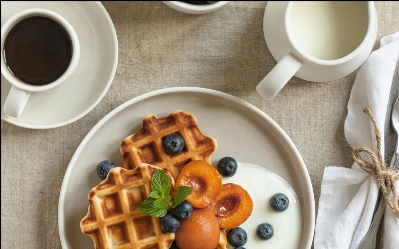 a plate of blueberries and waffles and a cup of coffee