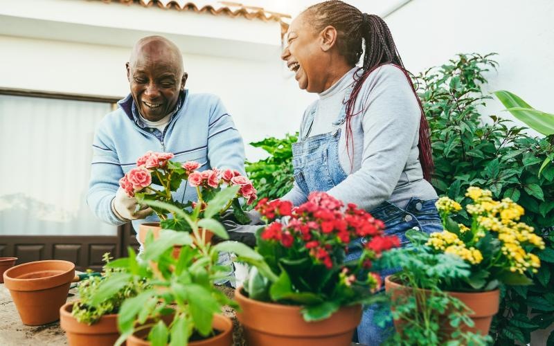 a man and woman laughing outside surrounded by potted flowers