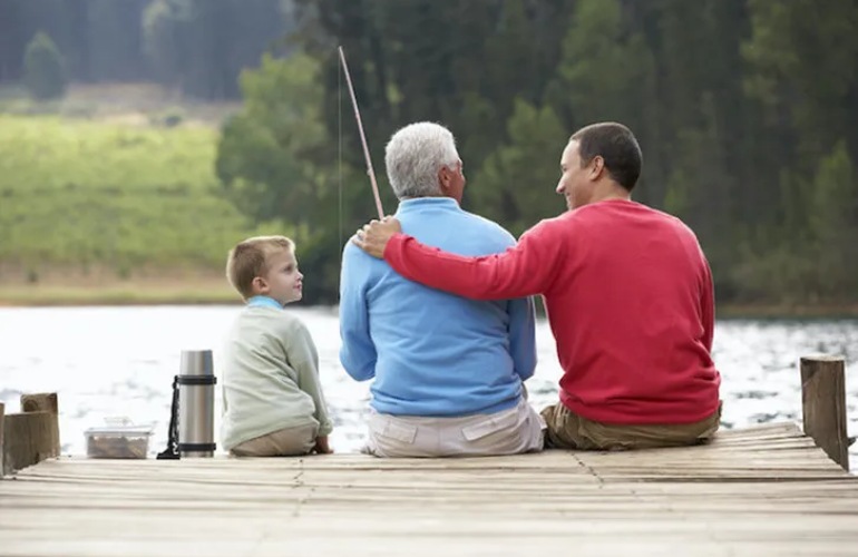 A father, son, and grandson sit on a dock fishing.