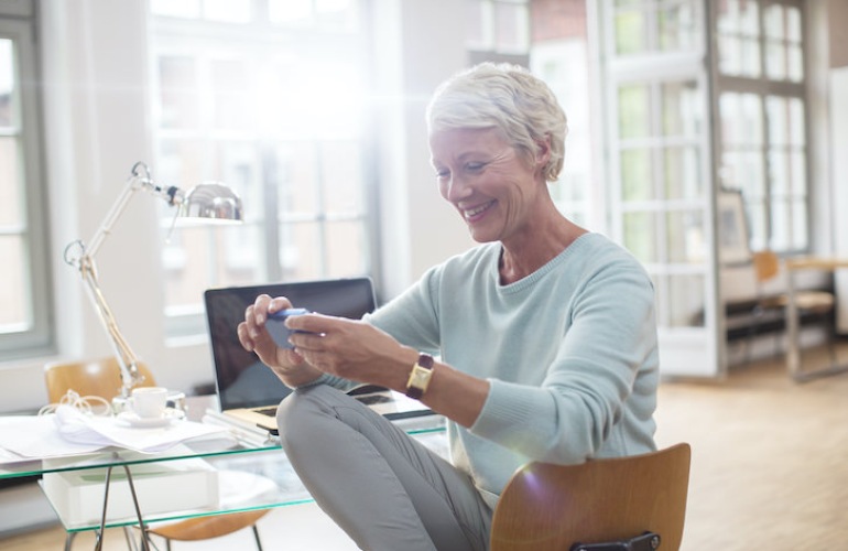 Senior adult woman looking at her phone while sitting at a desk.