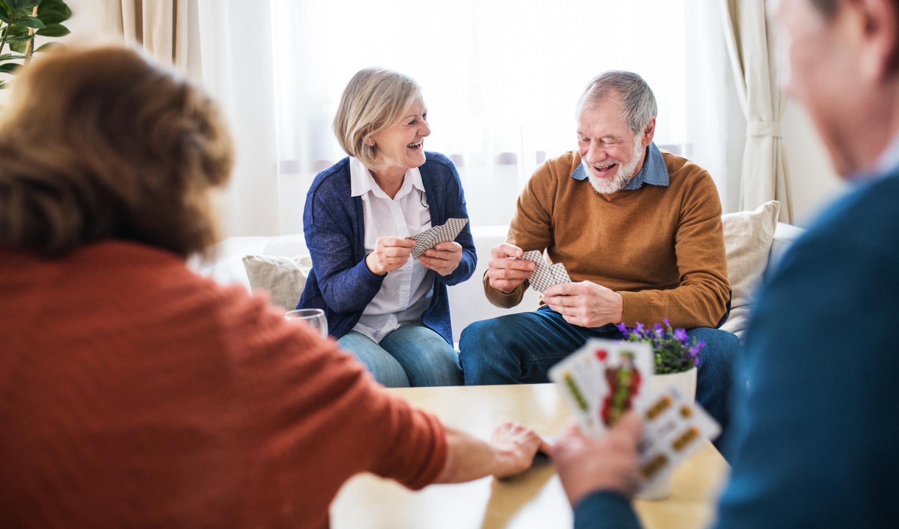 The essence of exceptional living Residents playing cards at Overture River District senior apartments in Fort Worth, TX, featuring flowers on the table.