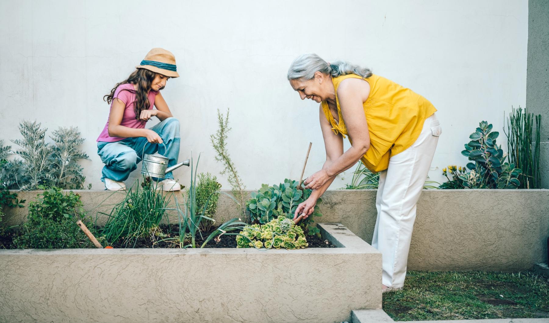 Your Joy to Embrace woman tends to a garden with her granddaughter