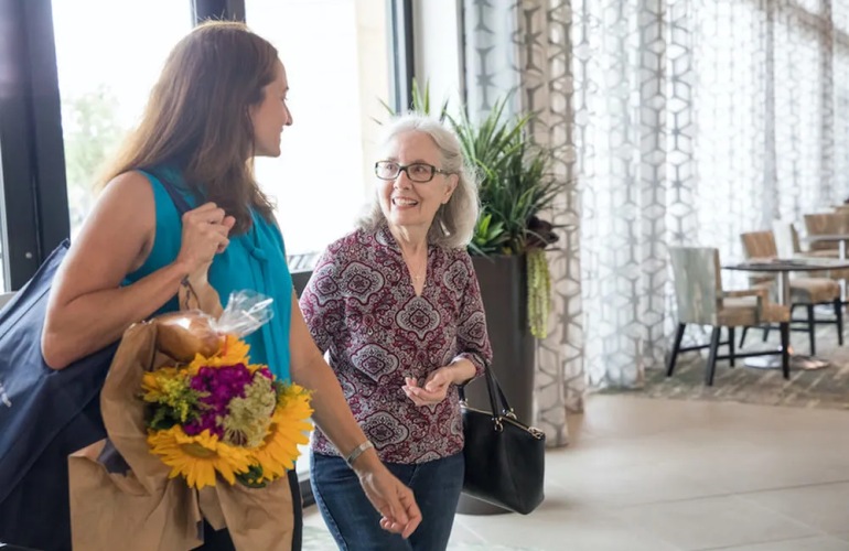 A senior adult woman and her adult daughter walk into an Overture lobby.