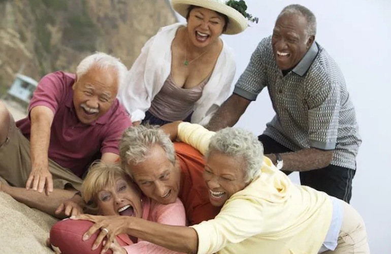 A group of senior adults playing football on a beach.