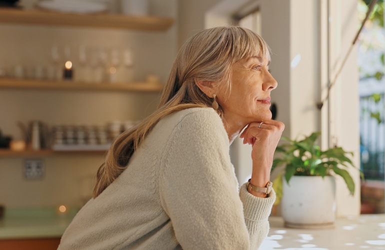 a person staring out the window leaning on a counter in a kitchen