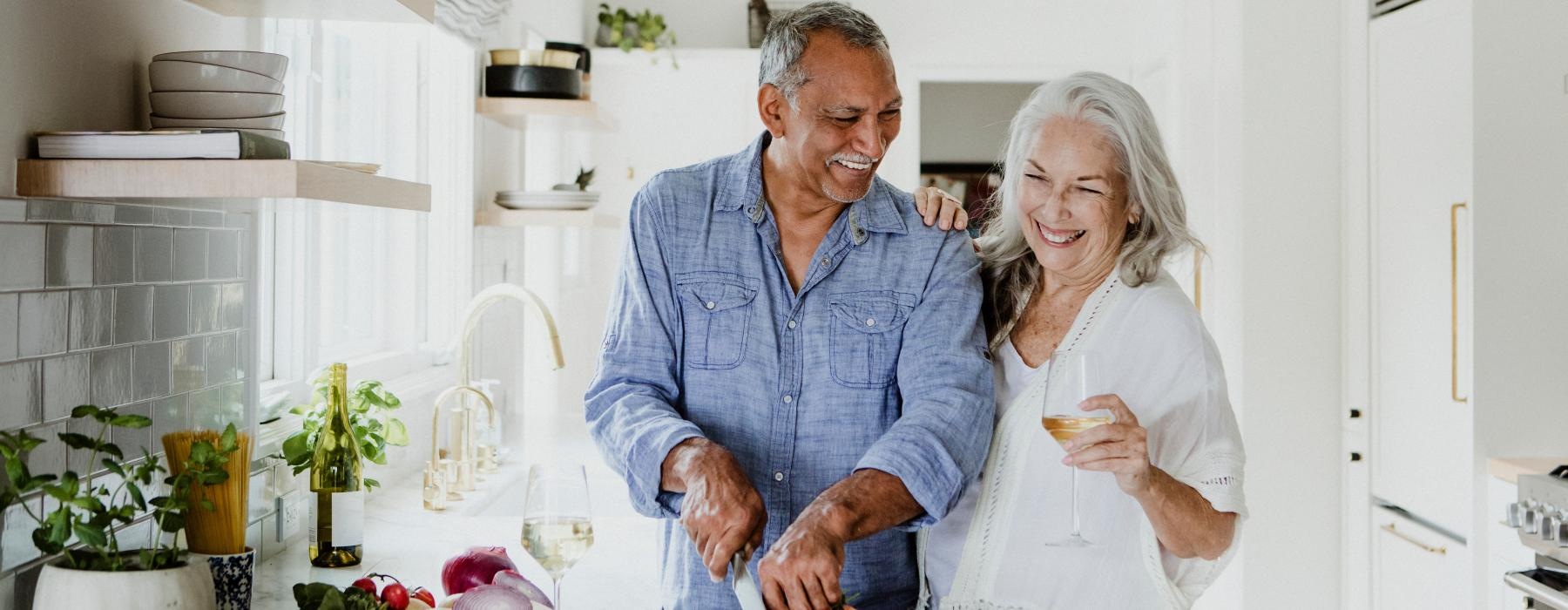 Couple smiling and cooking in a well lit kitchen 