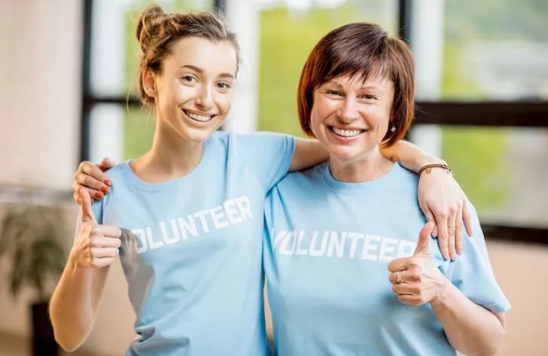 Two women wearing volunteer shirts and smiling at the camera.