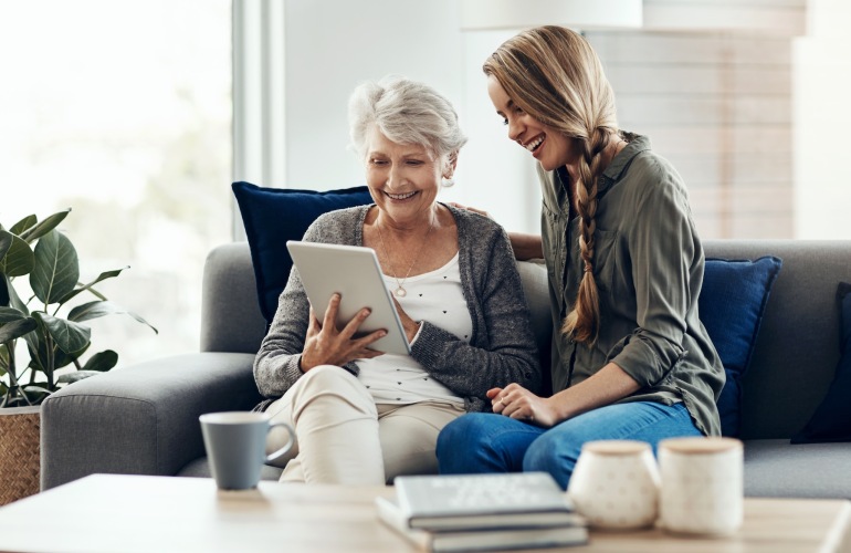 two women on a couch looking at a tablet and smiling