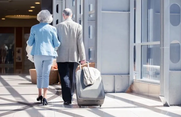 A senior adult couple rolling their luggage in an airport.