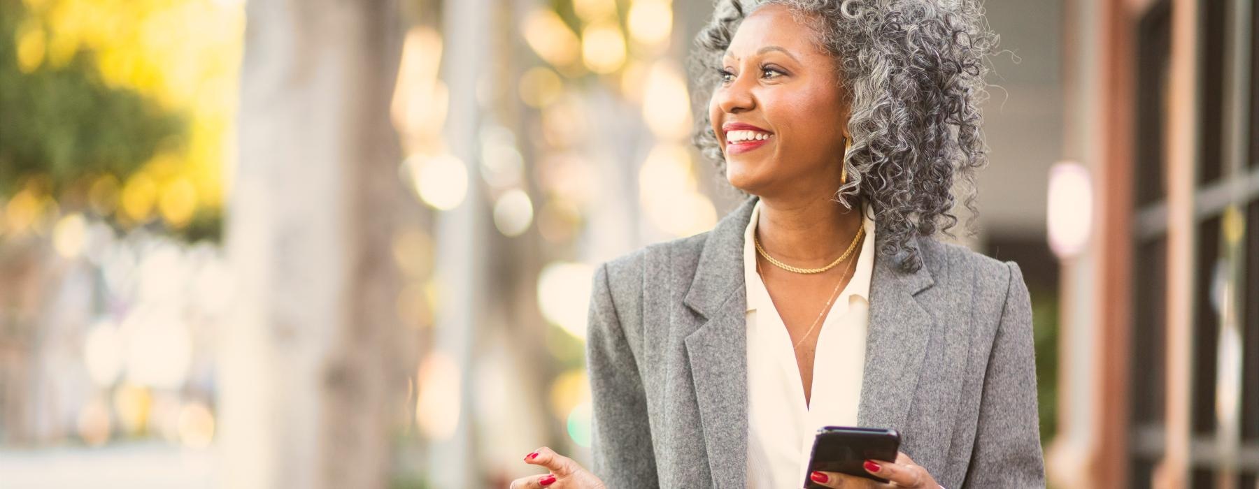 Woman walking on a sidewalk near shops smiling 