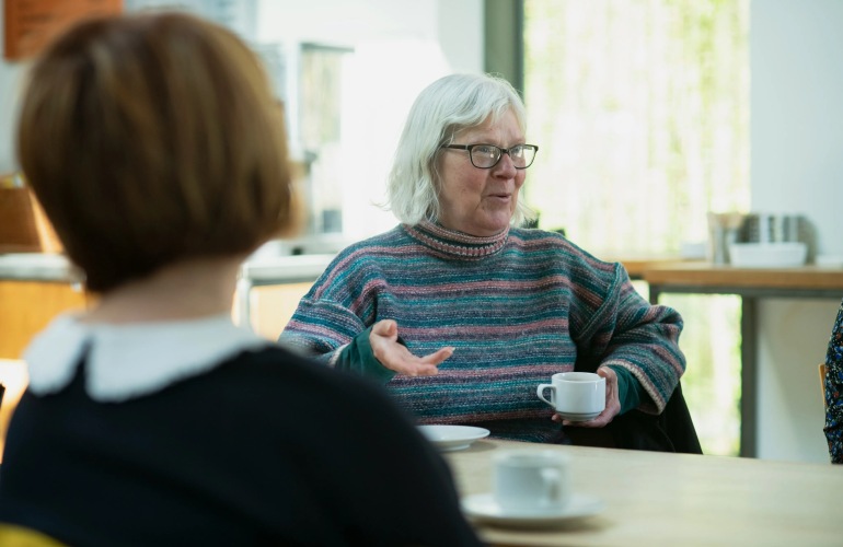 Group of senior adults talk around a table while drinking coffee.