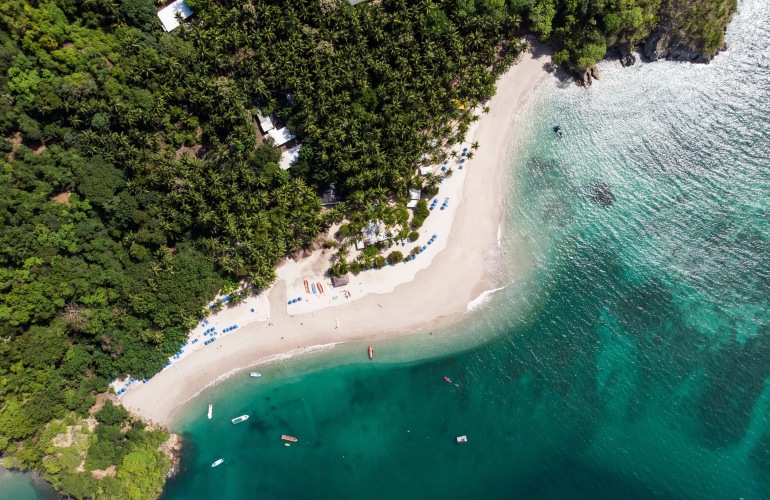 Aerial image of a white, sandy beach with crystal clear blue water.