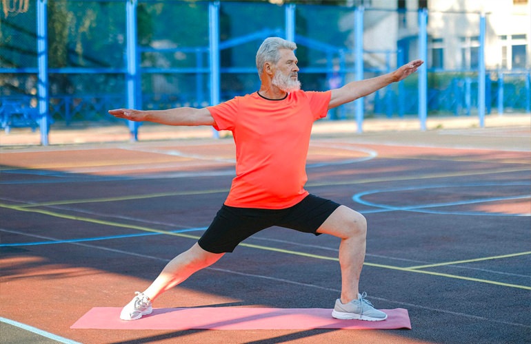 A senior man doing yoga outside on a sports court.