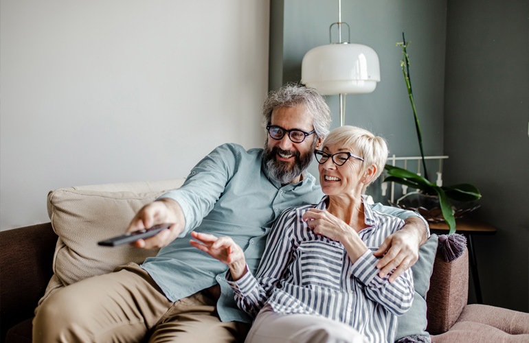 Senior adult couple sitting in their living room watching TV.