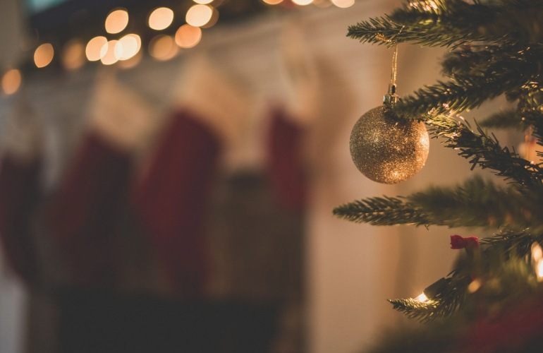 Close up of a glittery Christmas ornament hanging from a tree with stockings in the background.