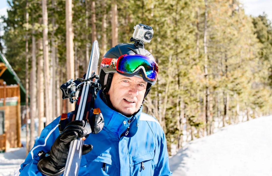 Senior man in a ski outfit holding his skis in front of a ski slope