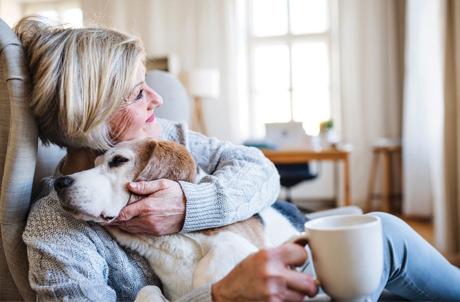 Senior woman sitting on a lounge chair with coffee and hugging her pet dog.
