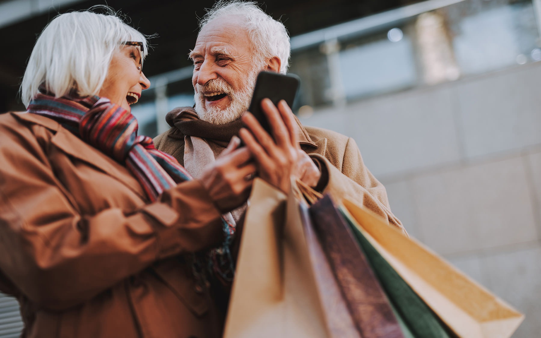 elderly couple with shopping bags smiling at each other and holding a phone