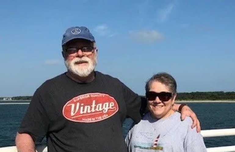 A senior adult standing on a dock in front of a body of water.