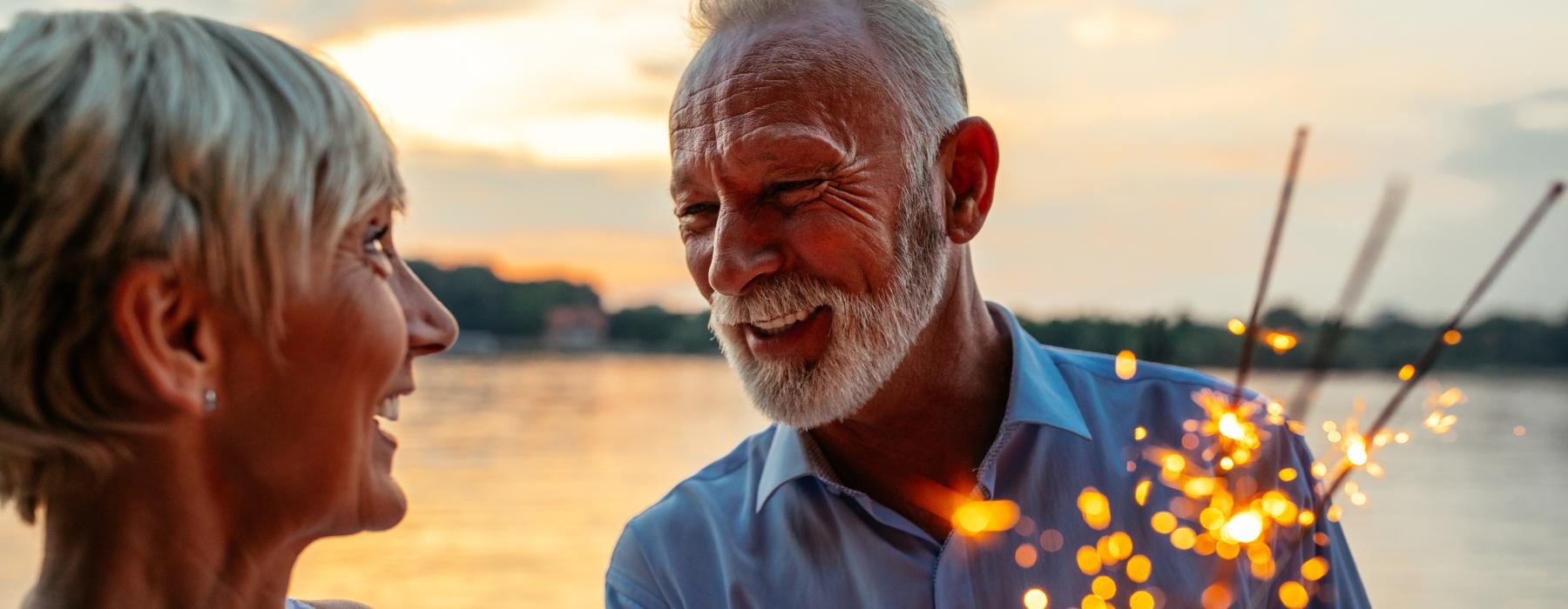 a man and woman holding sparklers near the water