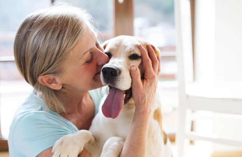 A senior adult woman hugs and kisses her pet dog.