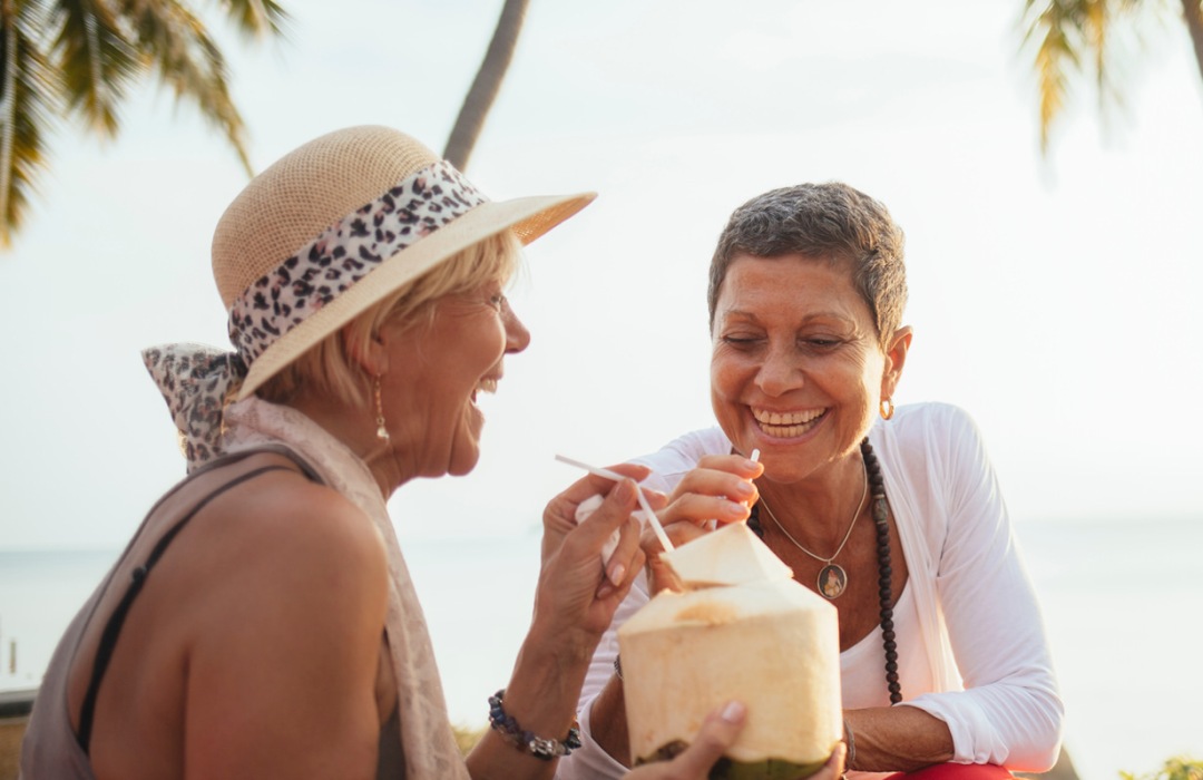 Two senior women sipping on a fruity drink on the beach