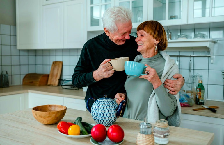 Senior adult couple having coffee in their kitchen and embracing each other.