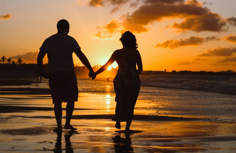 Silhouette of a couple walking along a beach at sunset.