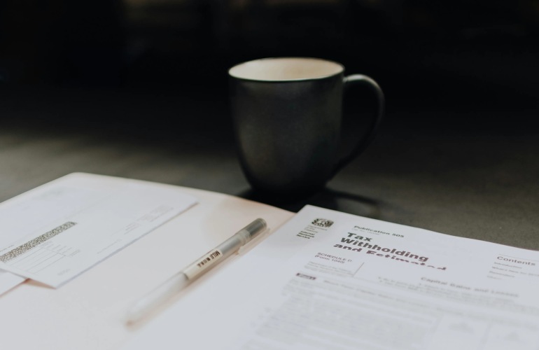 Tax forms in a folder with a pen, and a cup of coffee on a table.