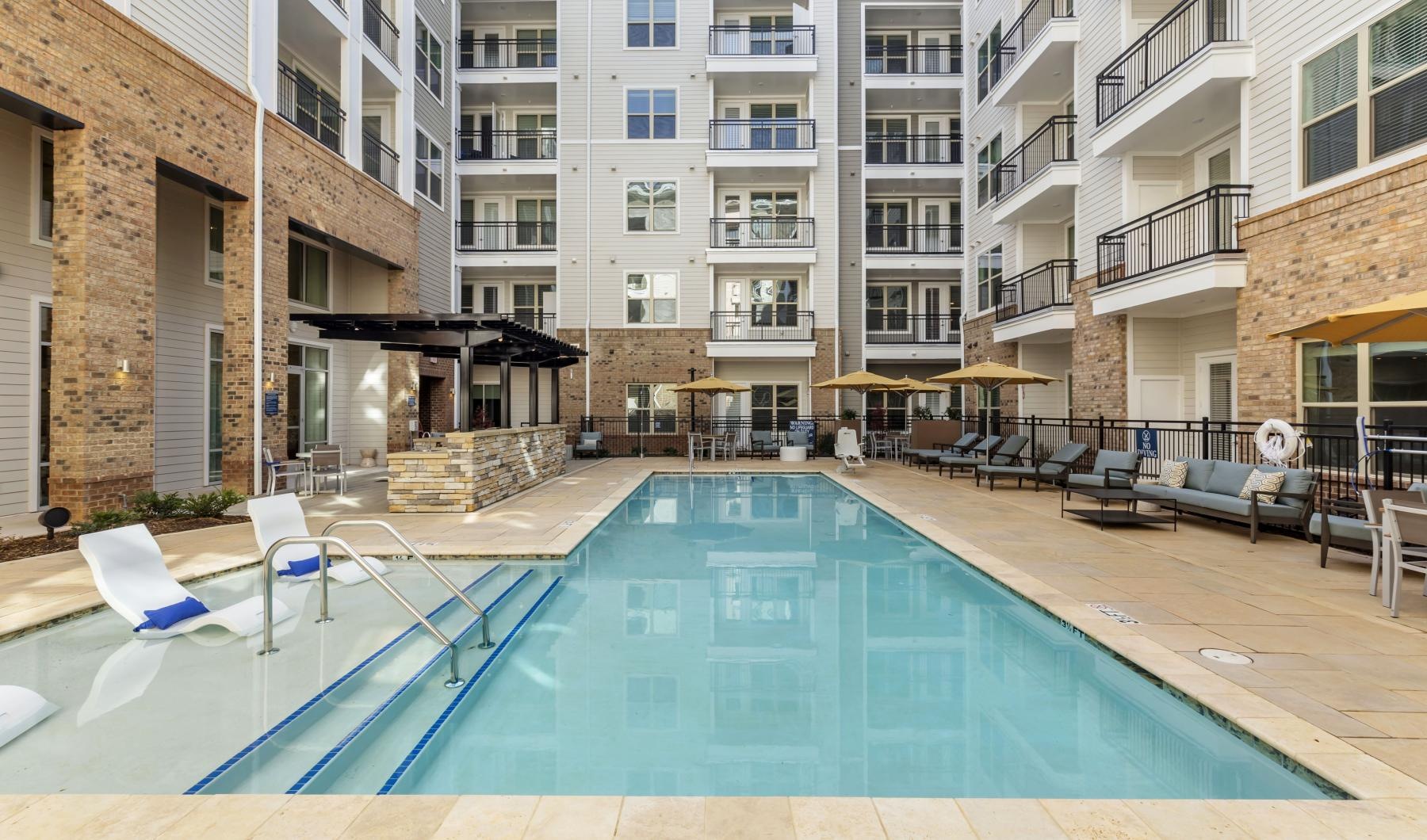 Large sparkling blue pool with a large deck and lounge chairs 