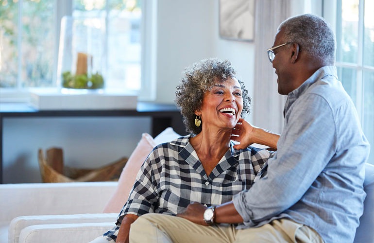 Senior adult couple talk on the couch in their living room.