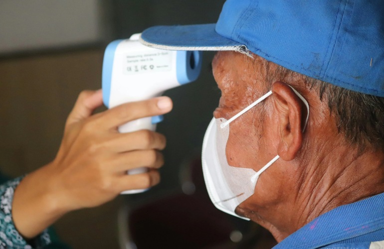 An adult senior man wearing a mask gets his temperature taken.