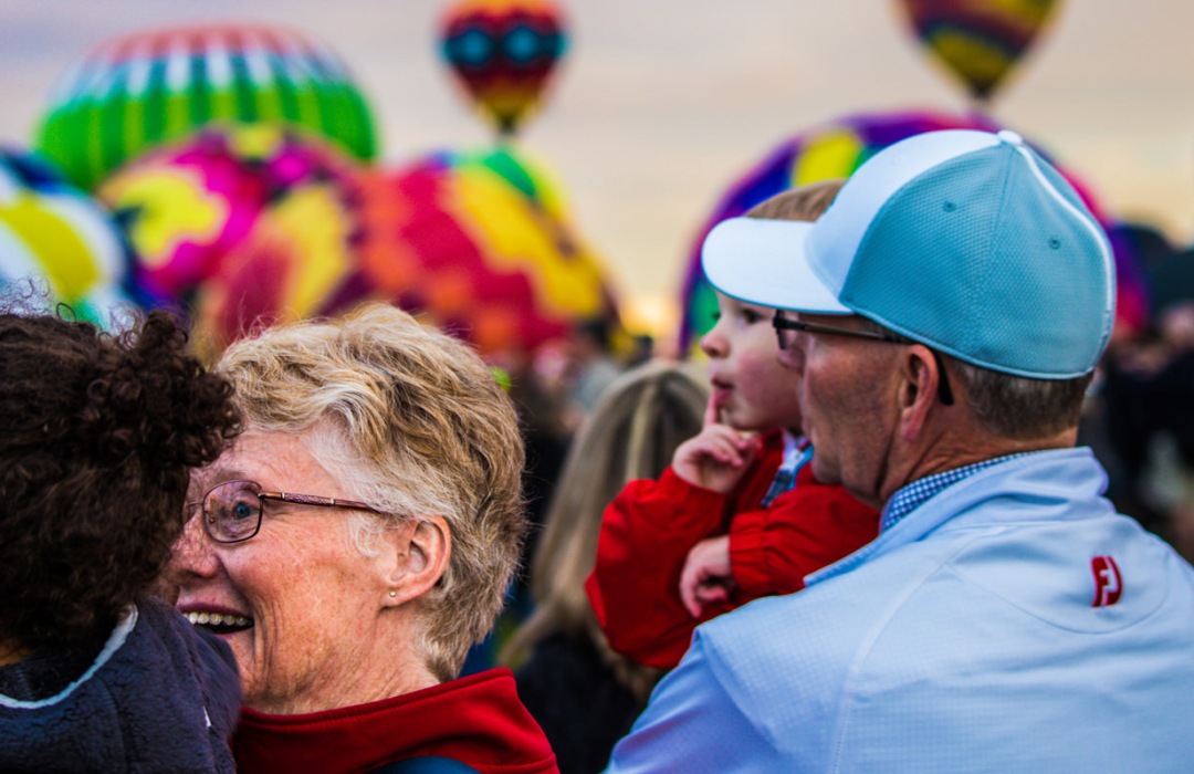 Grandparents hold their grandchildren while looking at hot air baloons in New Mexico.