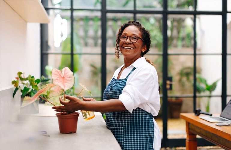 A senior adult woman watering her plants in her apartment.