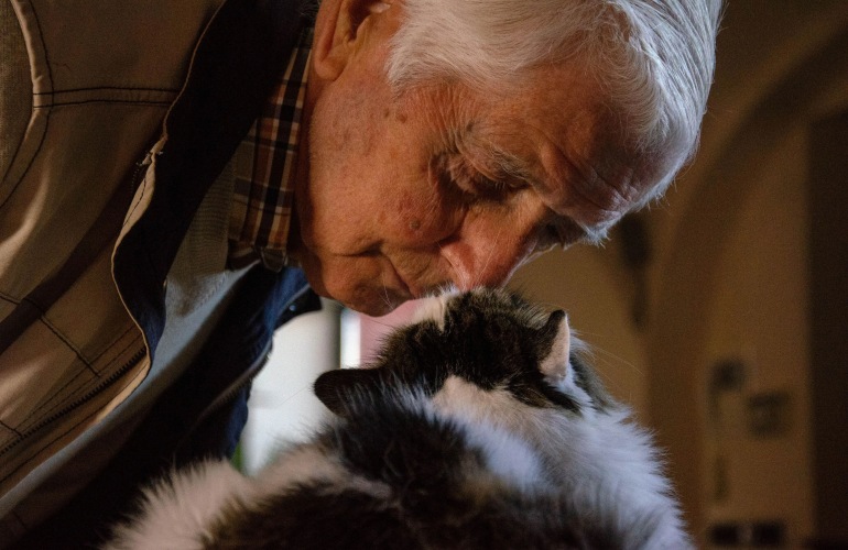 A senior adult man nuzzling his pet cat.