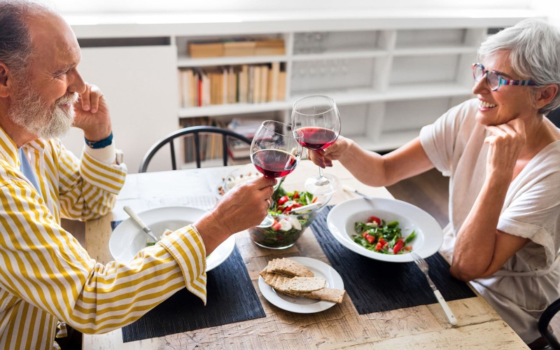 man and woman sitting across from each other eating dinner and toasting