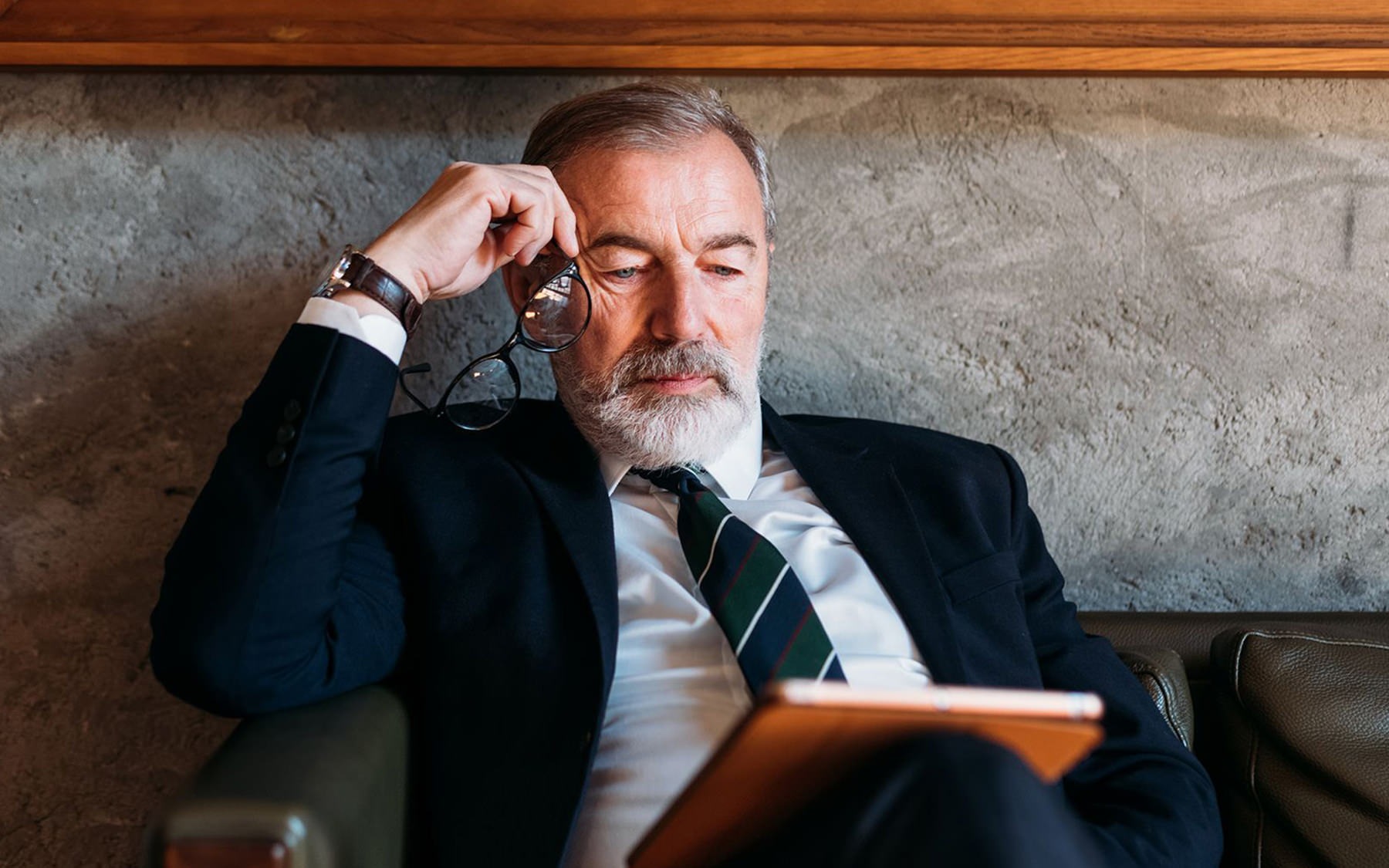 man in suit sitting in chair looking at a tablet device