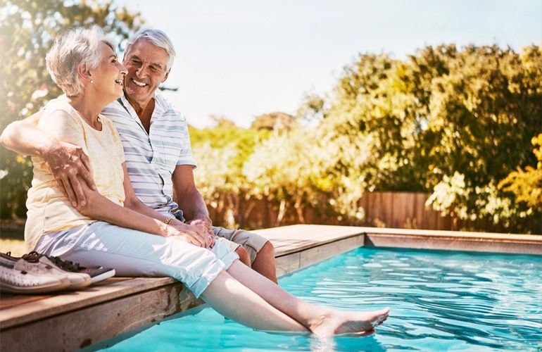 A senior couple sitting beside a pool with their feet wading in the water.