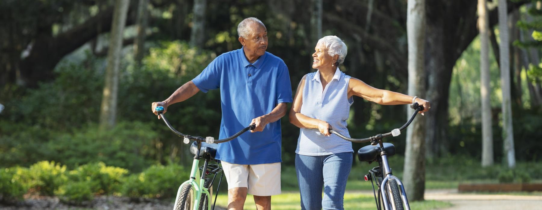 a couple walks their bicycles down a park road